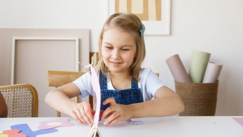 Free Young girl enjoying arts and crafts indoors, surrounded by colorful paper and art supplies, expressing creativity. Stock Photo