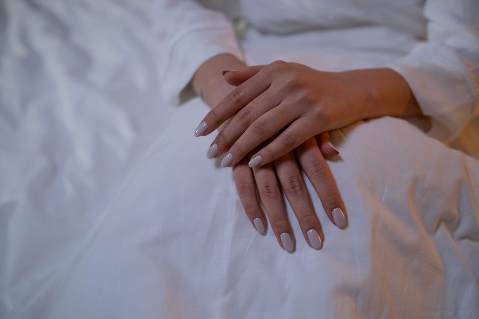 Close-up of hands resting, showcasing elegant nude nails on a white fabric.