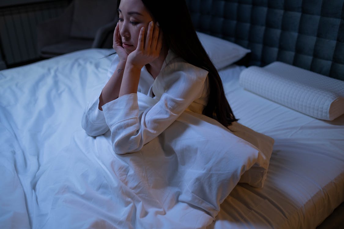 Free Woman in White Long Sleeve Shirt Sitting on a Bed Stock Photo