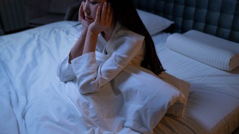 An Asian woman in bed at night, experiencing insomnia and loneliness, deep in thought.