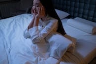 Woman in White Long Sleeve Shirt Sitting on a Bed