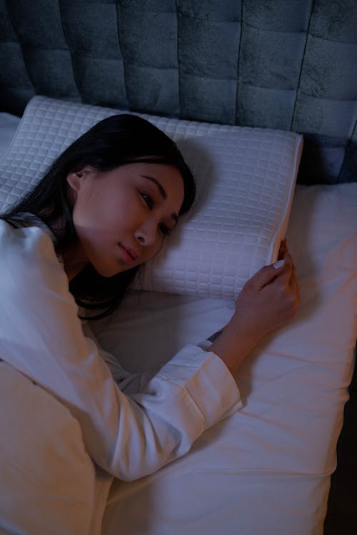 Free Woman in White Long Sleeve Shirt Lying on Bed Stock Photo