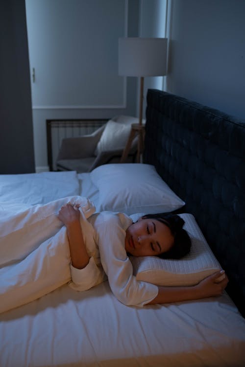 Free Woman in White Long Sleeve Shirt Lying on White Bed Stock Photo