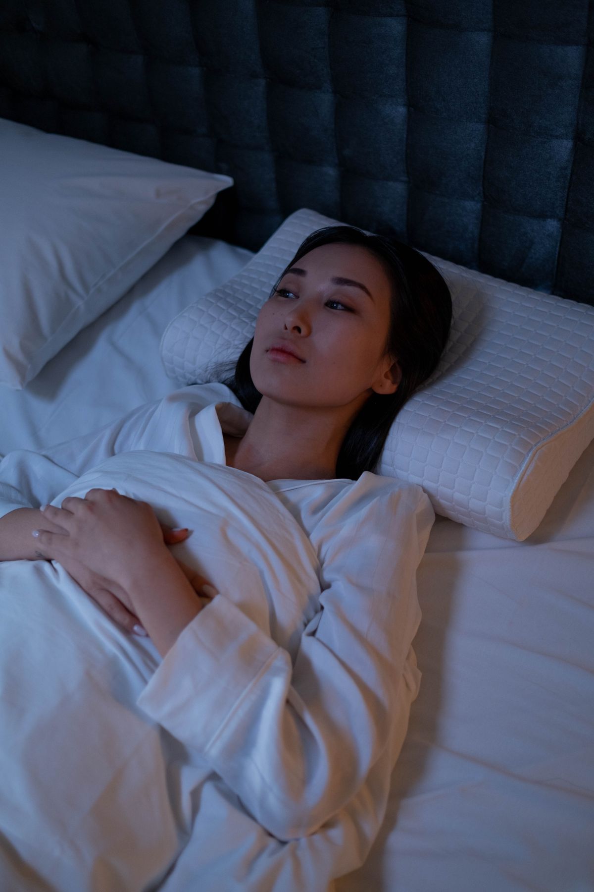 A woman lying awake in bed at night with her eyes open, alert despite being tired.
