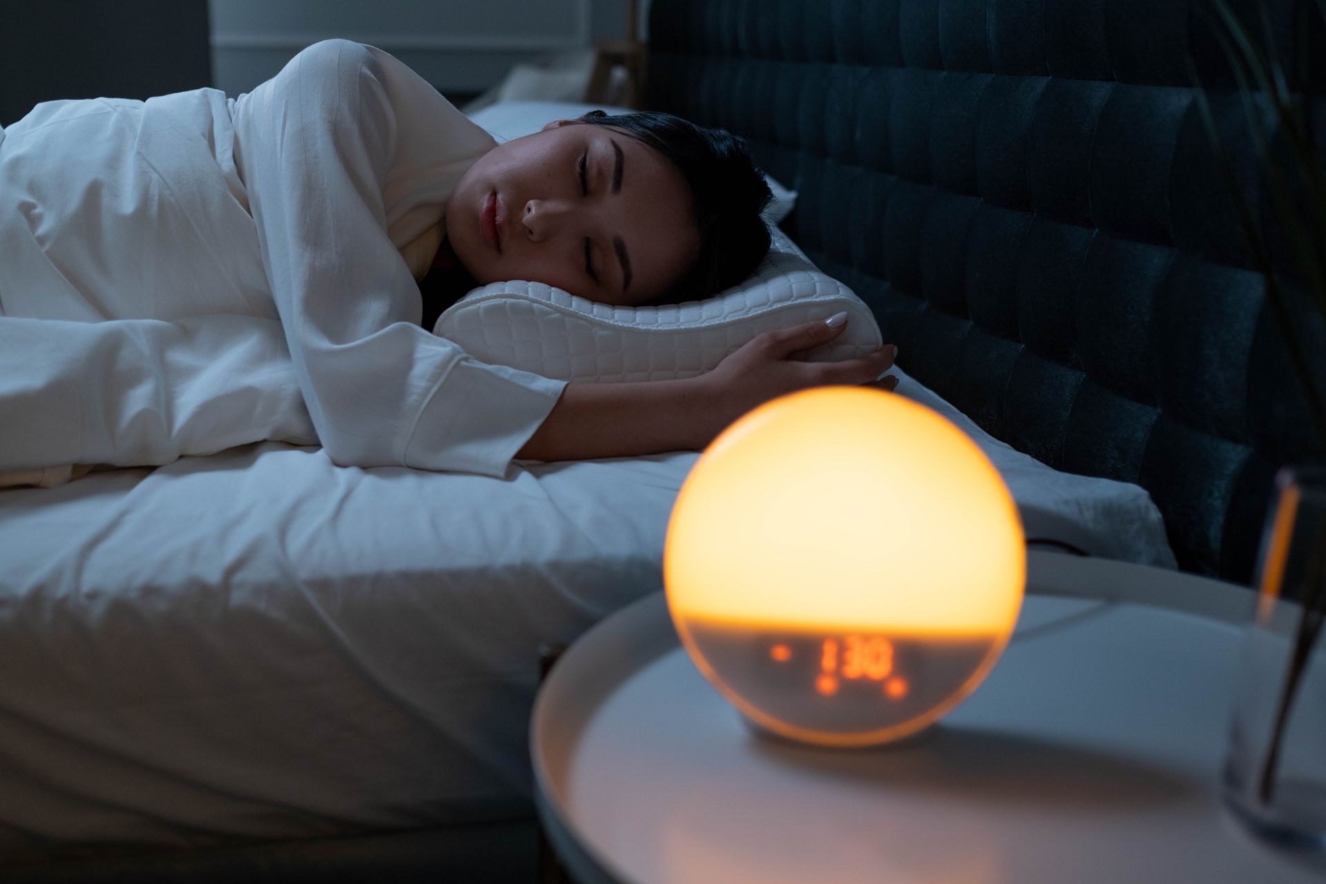 Woman sleeping peacefully in a cozy bedroom with ambient bedside light.