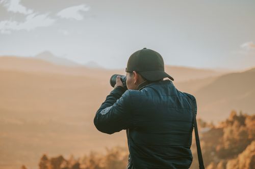 Free A man in a cap taking photos of a mountain landscape during the day, showcasing nature's beauty. Stock Photo