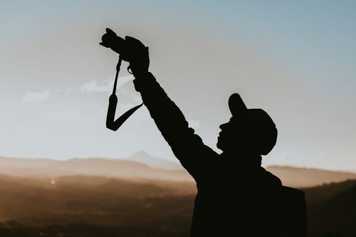 Free Silhouetted photographer takes a picture at sunrise, framed against a stunning mountain landscape. Stock Photo