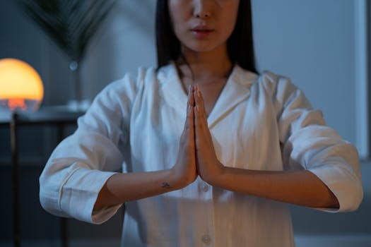 Woman meditating in a peaceful indoor setting, hands in prayer position, promoting wellness.