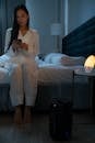 Woman in White Pajamas Sitting on Bed While Using a Phone