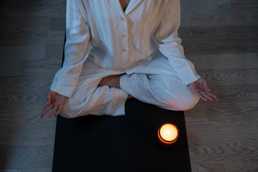 Serene meditation scene with a person in white pajamas and a glowing candle for relaxation.