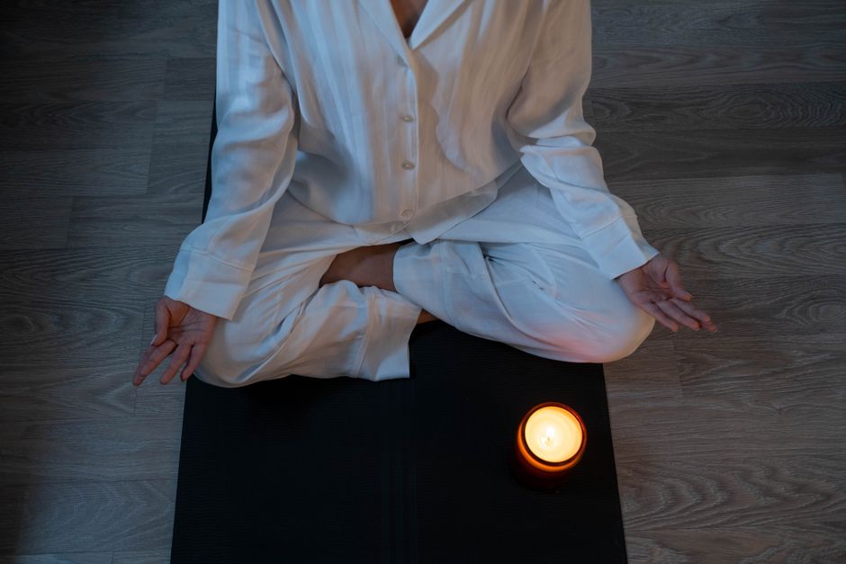 Como Criar um Ritual de Meditação para Mulheres Ocupadas 2 Serene meditation scene with a person in white pajamas and a glowing candle for relaxation.