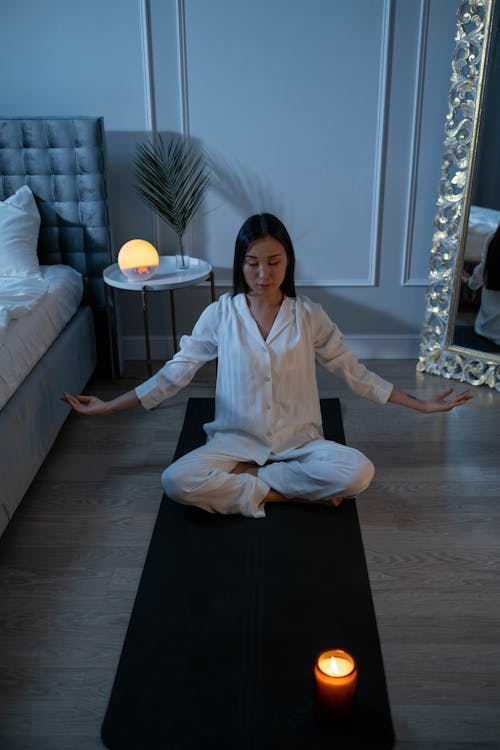 Free Woman in White Pajamas Meditating on a Yoga Mat Stock Photo