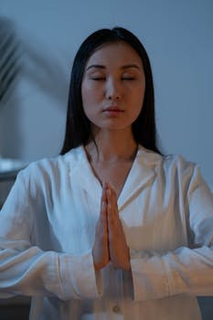 Asian woman meditating indoors, promoting peace and wellness.