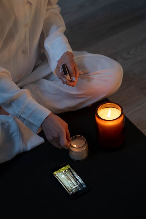 Free Person in white clothing lighting candles during a meditation session with a phone nearby, symbolizing modern mindfulness. Stock Photo