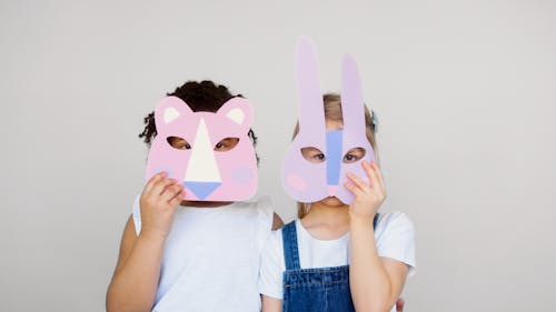 Free Two Kids Covering Their Faces With a Cutout Animal Mask Stock Photo