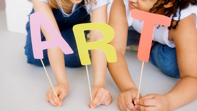Children playing with colorful paper cutouts spelling ART