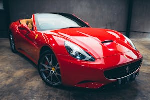 Expensive glossy red convertible with polished body parked in garage with concrete wall