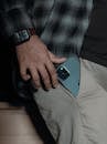 Crop unrecognizable male in casual clothes putting modern expensive smartphone in pocket of pants