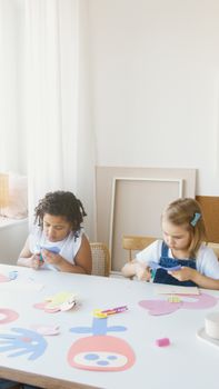 Two children creating colorful paper crafts indoors at a bright table.