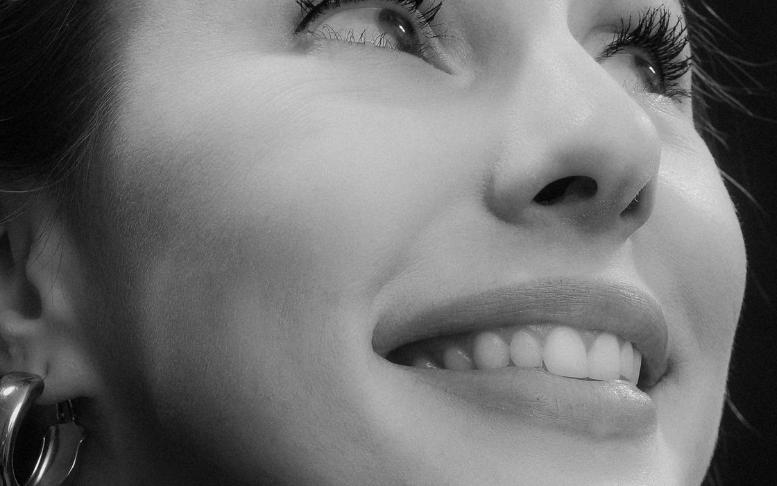 Elegant black and white portrait of a smiling woman gazing upwards in a studio setting.