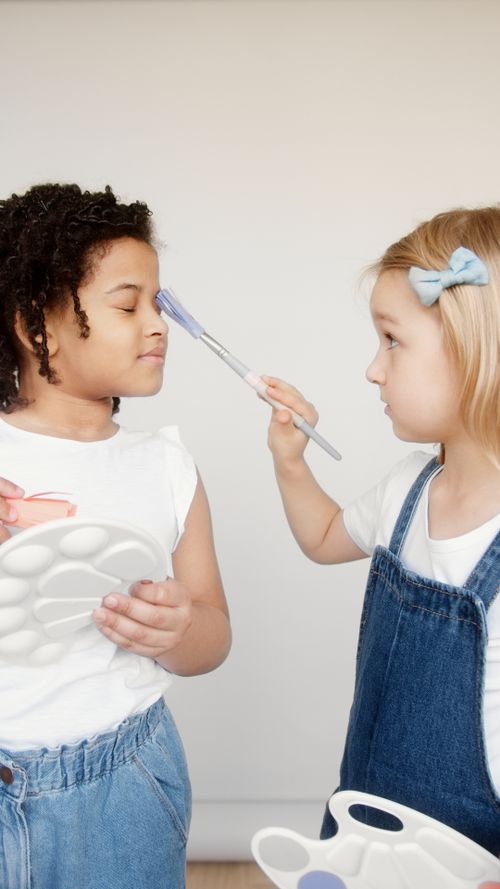 Free Two children enjoying a playful art activity indoors with paintbrushes. Stock Photo