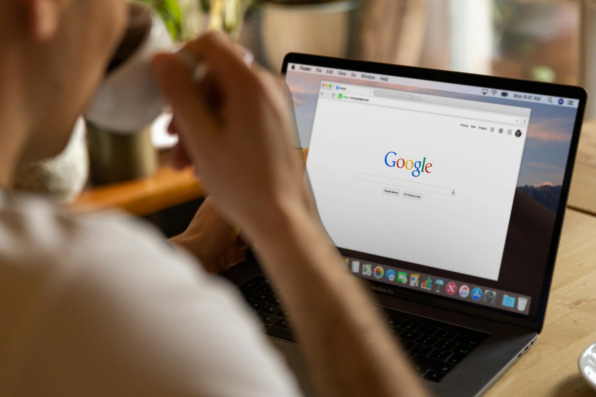 Close-up of an adult drinking coffee and browsing Google on a laptop indoors.