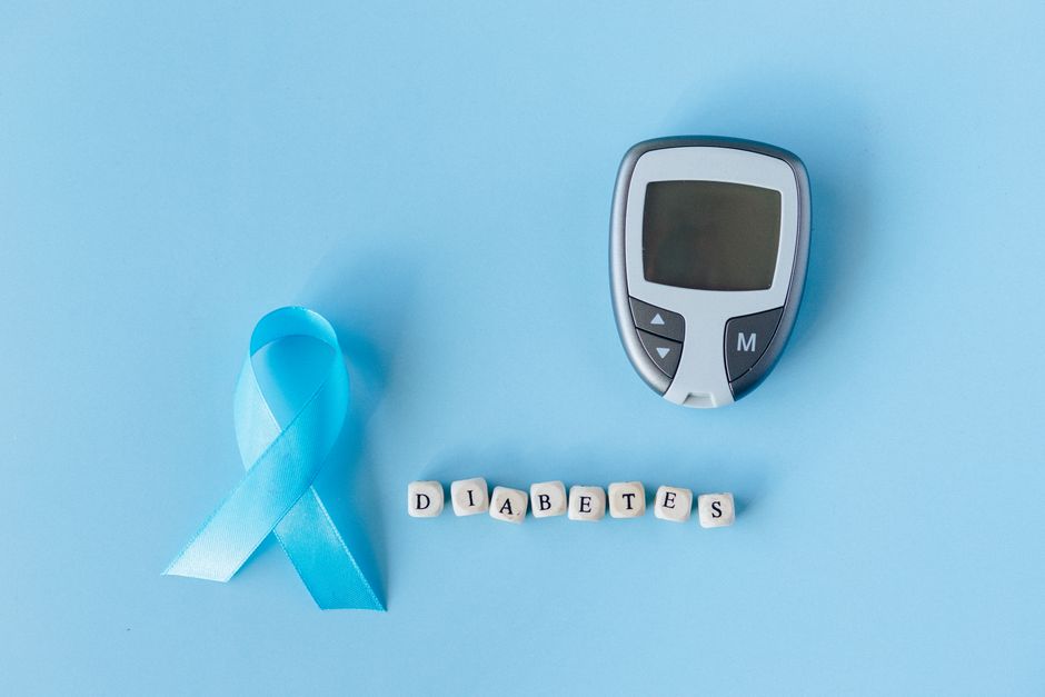 Blue ribbon and glucose meter on blue background highlighting diabetes awareness.