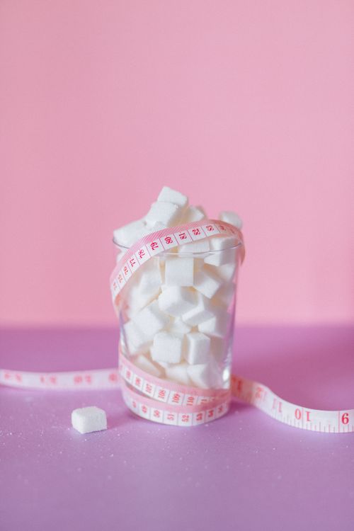 Free A glass of sugar cubes wrapped in measuring tape on a pink background symbolizes health awareness. Stock Photo