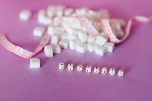 Sugar Cubes Beside Tape Measure Near Dices with Letter on a Pink Surface