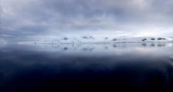 在多云的天空下，平静的海水映照出南极山脉