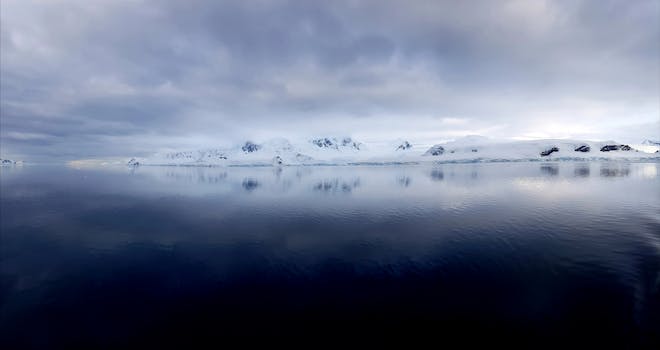 在多云的天空下，平静的海水映照出南极山脉