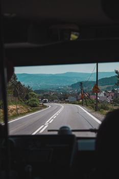 View of a mountain road from inside a bus, showing scenic countryside and hills.