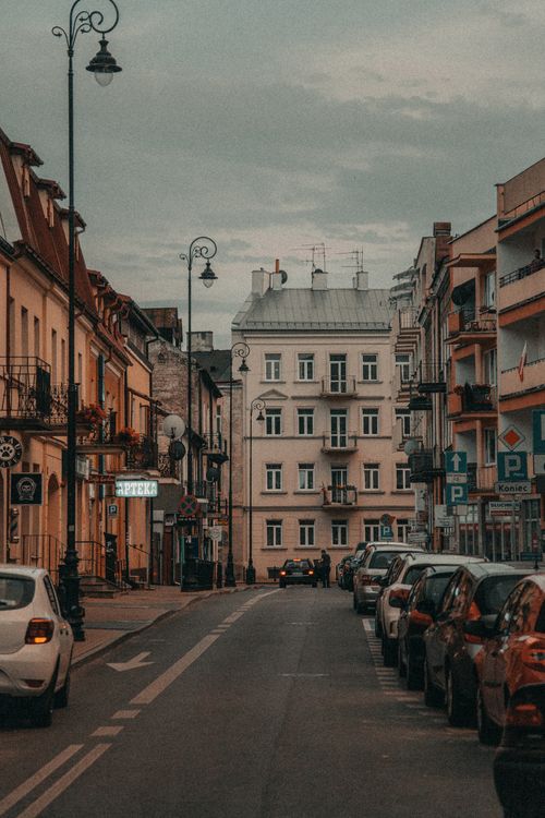 Free Asphalt road with automobiles parked between old buildings and houses under cloudy sky in town district Stock Photo