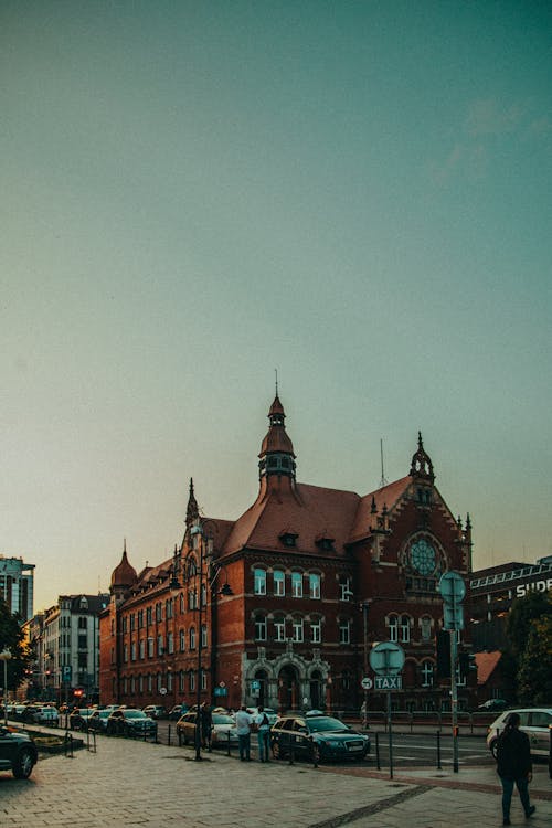 Exterior of colorful historic building with ornamental elements and towers located on street near road with cars in Katowice city