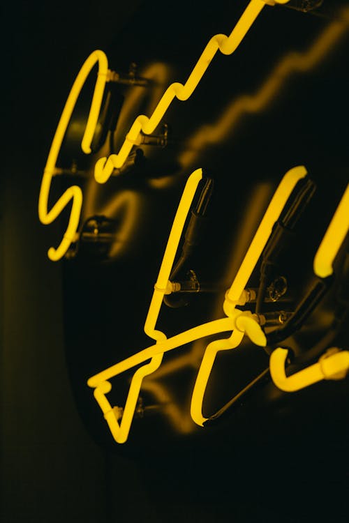 Creative bright neon signs signboard with inscription and yellow illumination attached to black wall in dark room of modern building