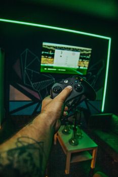 Unrecognizable tattooed male gamer with controller in hand playing video game in room with monitor and hookahs while spending time in modern club