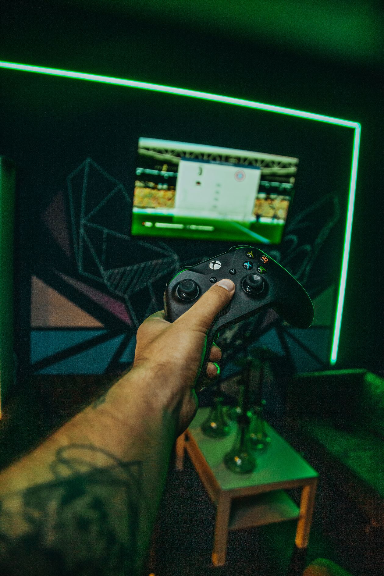 First-person view of a gamer holding a controller in a dark, neon-lit room facing a screen