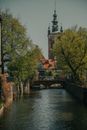 Calm water of channel between green trees leading to famous millers guild house with ornamental details on street of Gdansk
