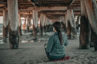Unrecognizable woman sitting on beach under bridge