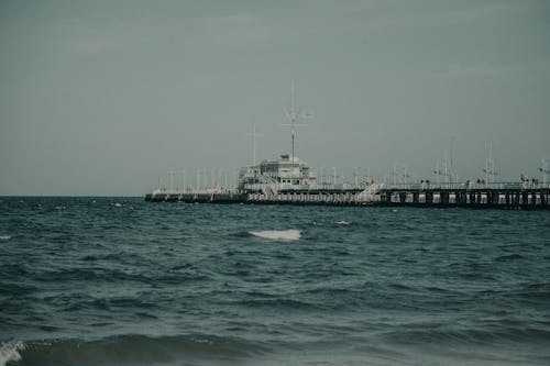 Contemporary big ship floating on rippling seawater near harbor with metal constructions in coastal terrain against cloudless sky in nature