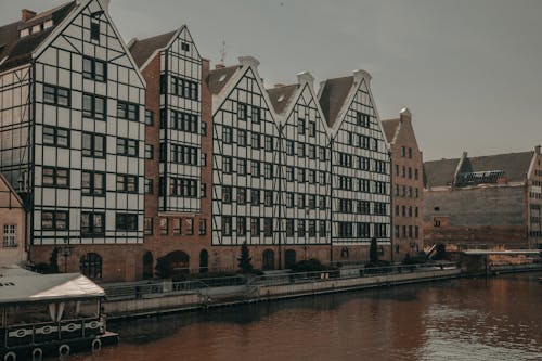 Exteriors of typical aged residential buildings located on river shore against overcast sky in Gdansk