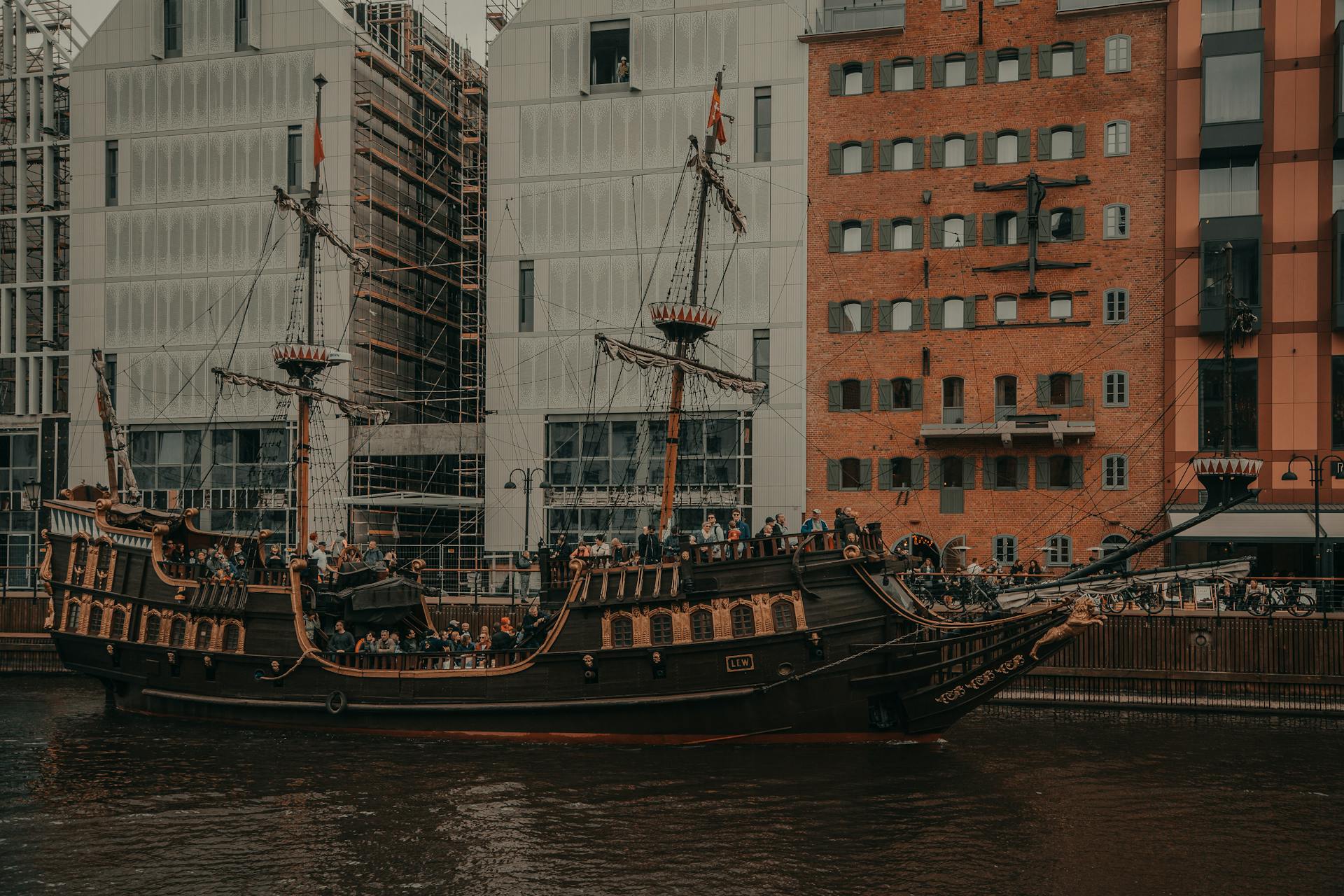Old ship sailing on river near residential buildings in city