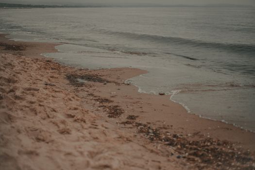 Picturesque view of rippling sea with foamy waves rolling on sandy beach against gloomy sky