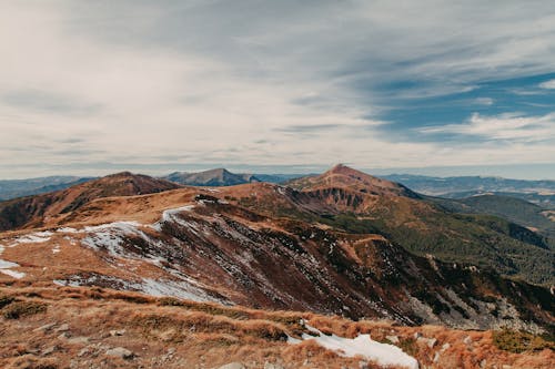 Amazing scenery of massive rocky mountain range covered with dry grass and snow against cloudy sky