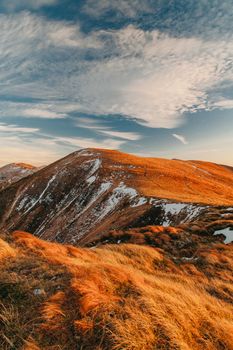 Stunning sunrise view over a snow-capped mountain ridge with golden grass and dramatic clouds.
