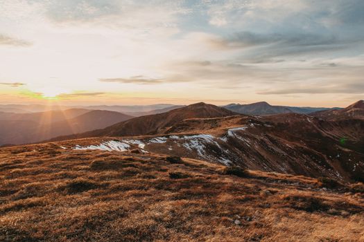 Scenic mountain landscape with sun setting over the horizon casting warm rays across the terrain.