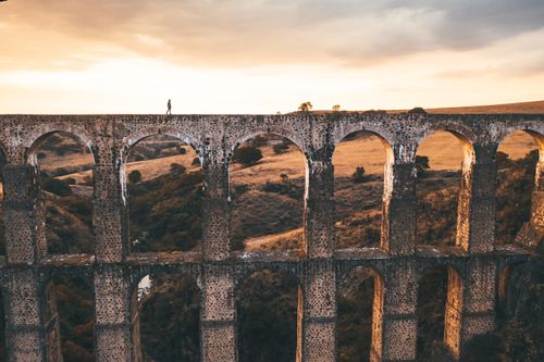 Free A stunning view of the historic Arcos del Sitio aqueduct in Mexico with a person walking at sunset. Stock Photo