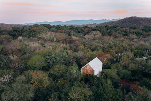 A serene aerial shot of a house surrounded by lush trees and rolling hills at twilight, capturing natural beauty.