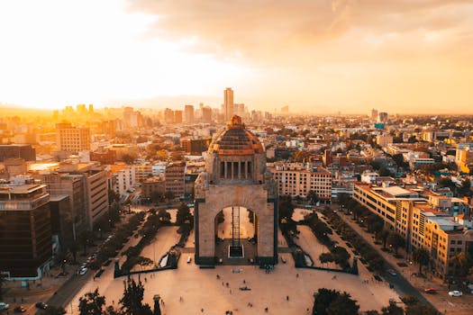 A stunning aerial view of Mexico City's urban landscape at sunset, featuring the iconic Revolution Monument.