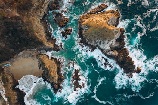 A breathtaking aerial shot featuring dramatic rock formations and waves along a rugged coastline.